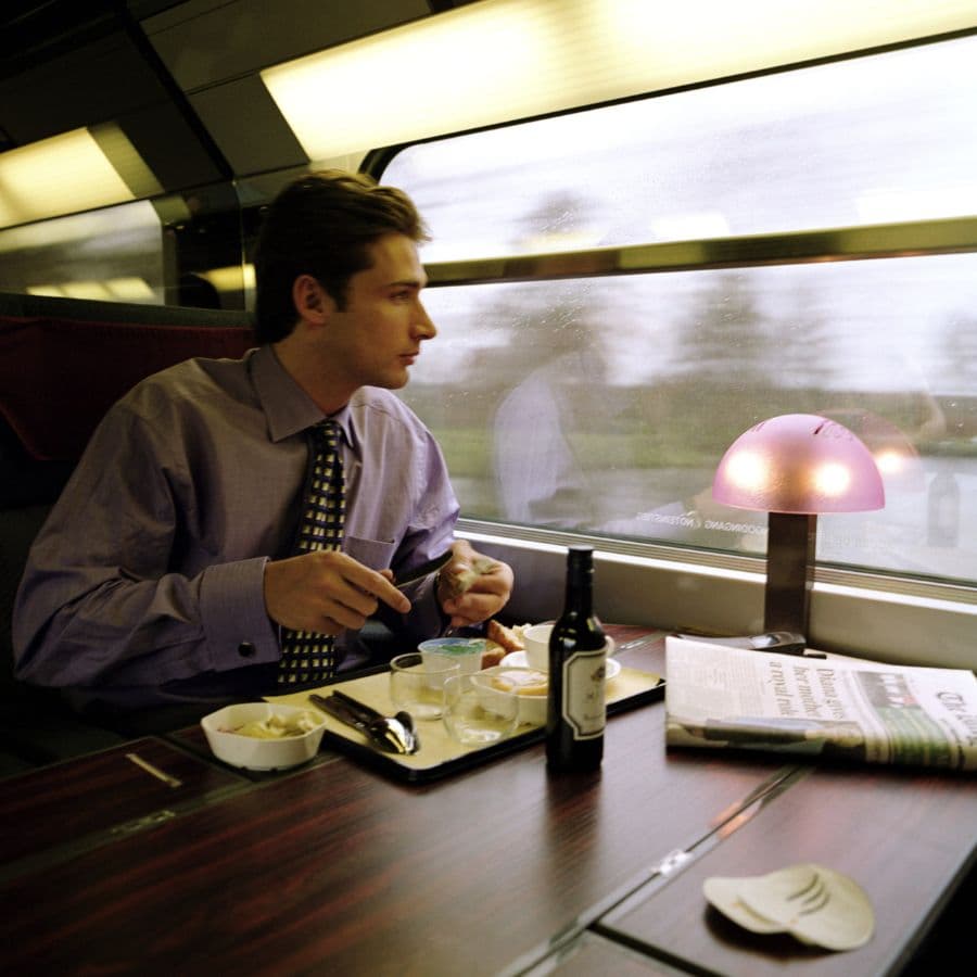 A man in a suit eats a meal while sitting in a train, looking out the window.
